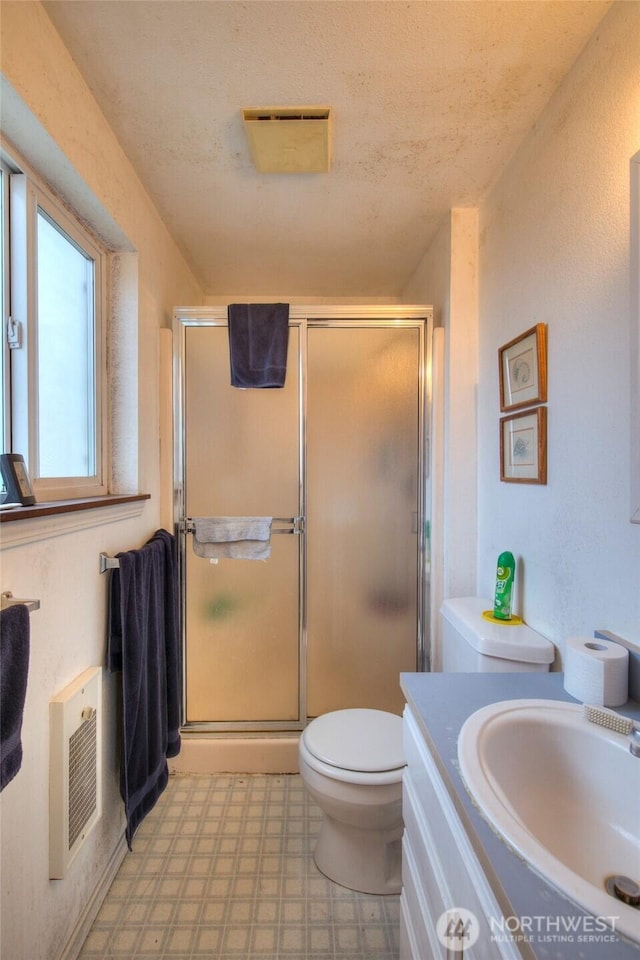 bathroom with heating unit, vanity, an enclosed shower, and a textured ceiling