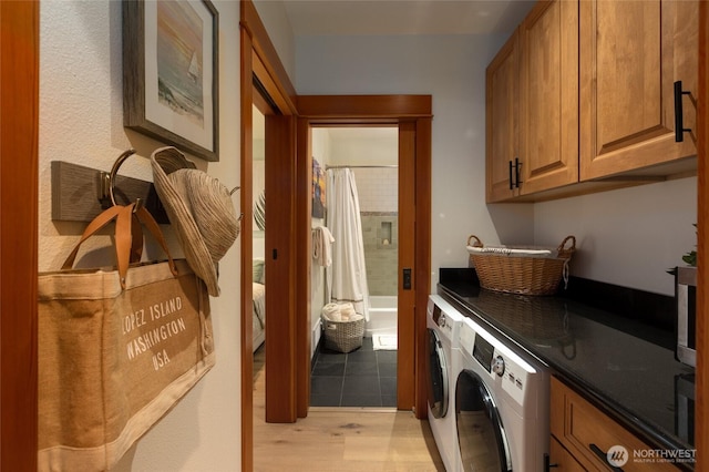 clothes washing area with light wood-style flooring, washer and clothes dryer, and cabinet space