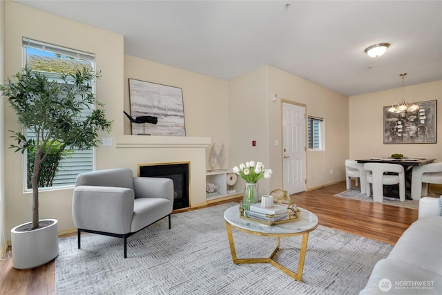 living area featuring a chandelier, a glass covered fireplace, baseboards, and wood finished floors