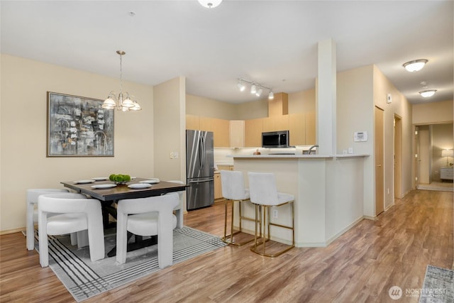 dining room featuring a notable chandelier, light wood-style flooring, rail lighting, and baseboards