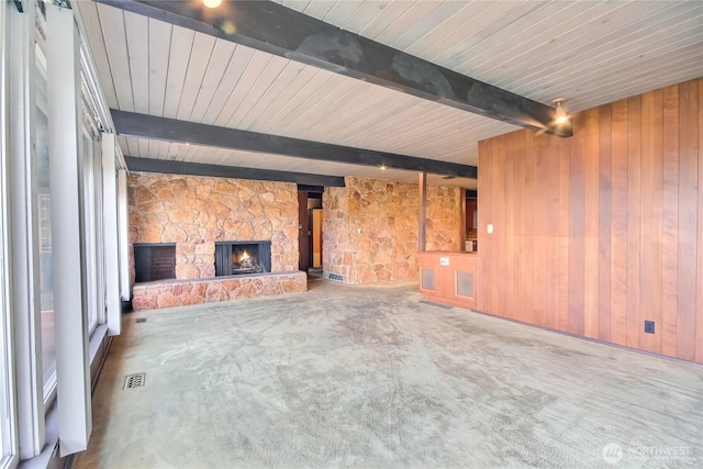 unfurnished living room with wooden walls, beam ceiling, visible vents, and a stone fireplace