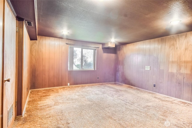 carpeted spare room with wood walls, visible vents, baseboards, and a textured ceiling