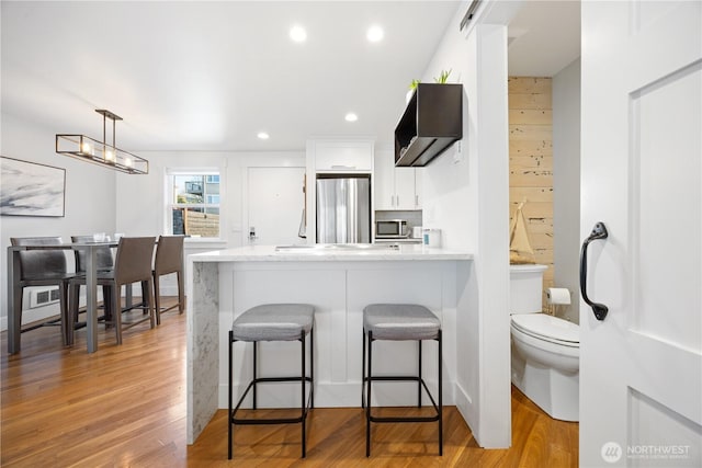 kitchen featuring light stone counters, light wood finished floors, appliances with stainless steel finishes, white cabinets, and a peninsula