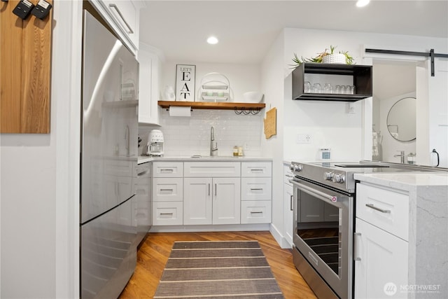 kitchen with light wood finished floors, tasteful backsplash, a barn door, white cabinets, and appliances with stainless steel finishes