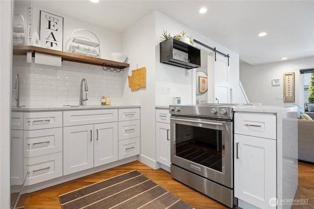 kitchen featuring a barn door, a sink, white cabinetry, light countertops, and stainless steel electric range oven