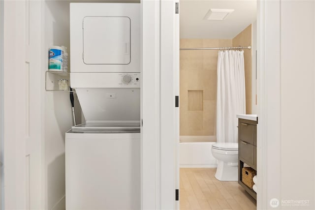 full bath featuring toilet, wood finished floors, vanity, stacked washing maching and dryer, and shower / bath combination with curtain