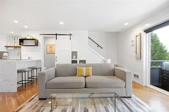 living area with a barn door, light wood-type flooring, visible vents, and recessed lighting