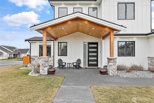 view of exterior entry featuring board and batten siding, stone siding, and a yard