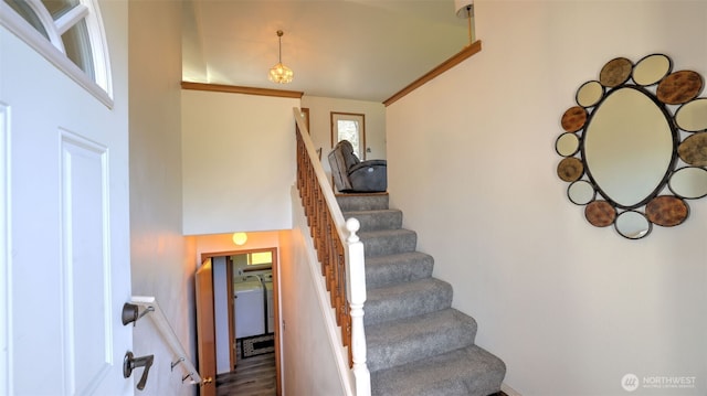 stairs with ornamental molding, washer / clothes dryer, a towering ceiling, and wood finished floors