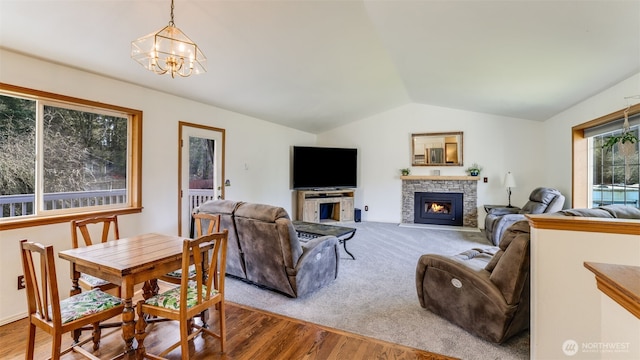 living room with vaulted ceiling, a stone fireplace, wood finished floors, and a chandelier