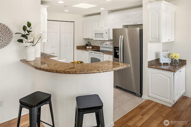 kitchen featuring white appliances, white cabinets, a peninsula, a kitchen bar, and a sink