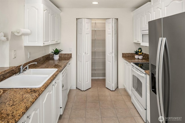 kitchen featuring light tile patterned floors, white appliances, a sink, and white cabinets