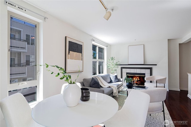 dining area with baseboards, dark wood-style flooring, a tile fireplace, and track lighting