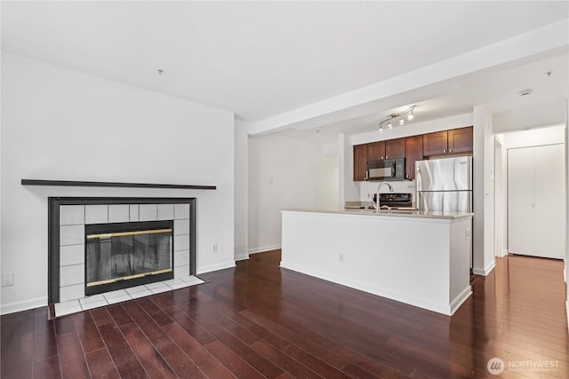 kitchen featuring a tiled fireplace, dark wood-type flooring, freestanding refrigerator, light countertops, and black microwave