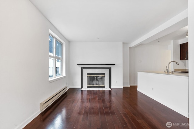 unfurnished living room featuring baseboards, a fireplace, a baseboard heating unit, and dark wood finished floors