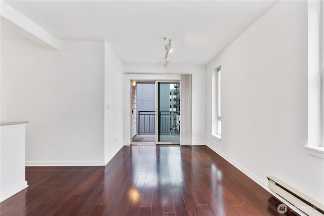 unfurnished room featuring dark wood-style flooring, a baseboard radiator, rail lighting, and baseboards