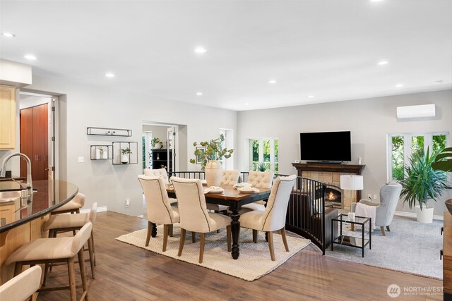 dining room with a warm lit fireplace, recessed lighting, wood finished floors, baseboards, and a wall mounted AC