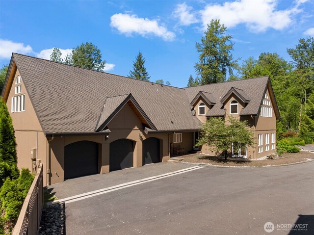 view of front of property featuring driveway, roof with shingles, an attached garage, and stucco siding