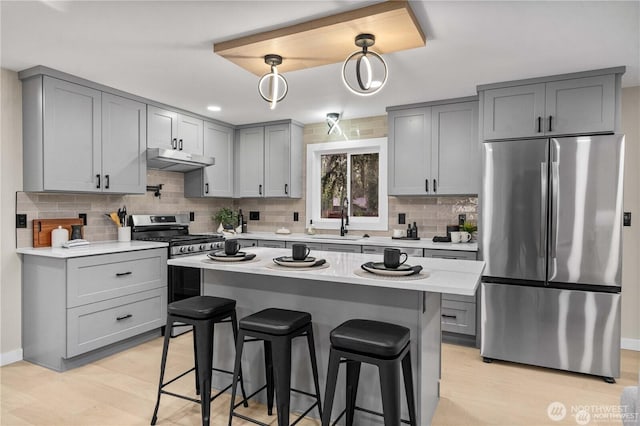 kitchen with light wood-type flooring, a breakfast bar, decorative light fixtures, sink, and appliances with stainless steel finishes