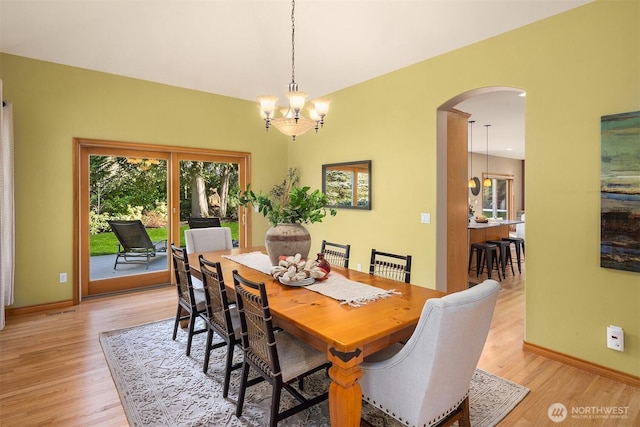 dining room with arched walkways, baseboards, an inviting chandelier, and light wood-style floors