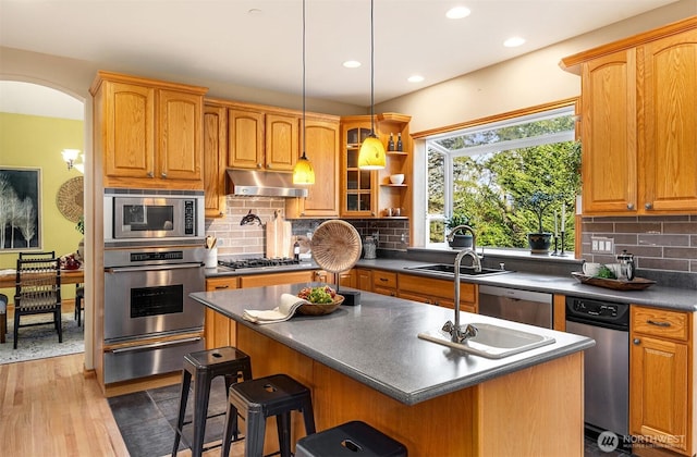 kitchen with dark countertops, stainless steel appliances, under cabinet range hood, a sink, and a warming drawer