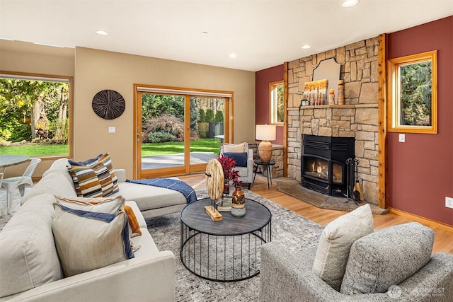 living area with a wealth of natural light, recessed lighting, wood finished floors, and a stone fireplace