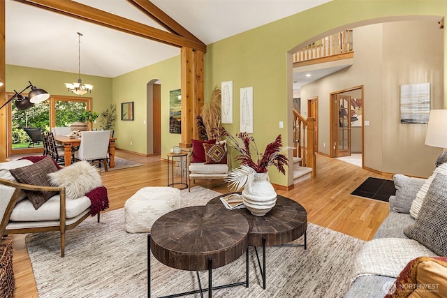 living room featuring light wood finished floors, arched walkways, stairway, vaulted ceiling, and a notable chandelier