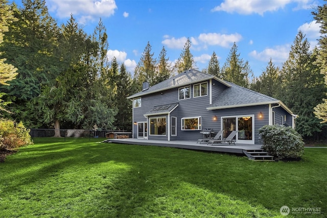 rear view of property featuring a yard, a chimney, a shingled roof, fence, and a deck