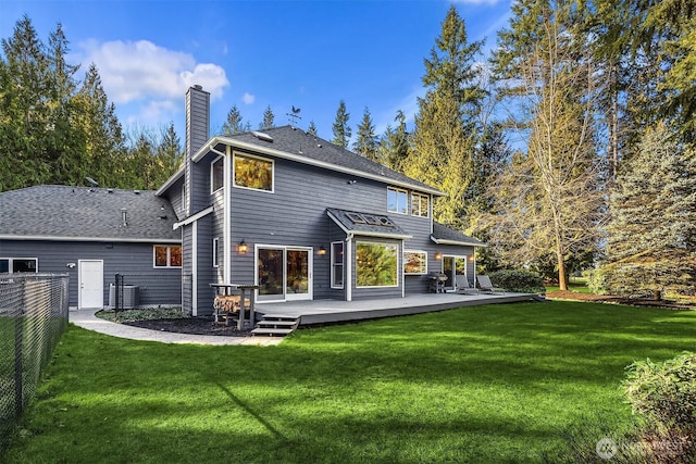 back of property with a chimney, fence, a deck, and a lawn