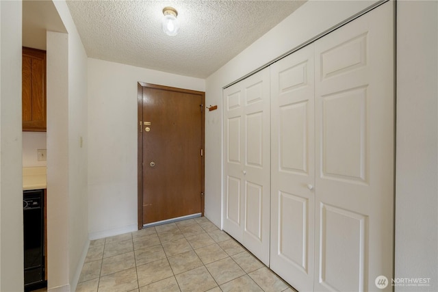 hall featuring light tile patterned floors, baseboards, and a textured ceiling