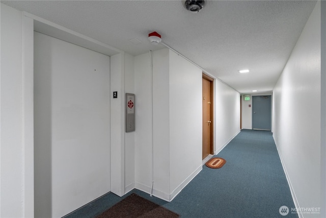 hall with a textured ceiling, dark colored carpet, and baseboards