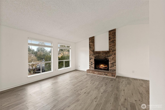 unfurnished living room with lofted ceiling, a textured ceiling, a fireplace, and wood finished floors