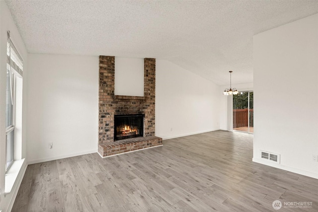 unfurnished living room with wood finished floors, visible vents, vaulted ceiling, a brick fireplace, and an inviting chandelier