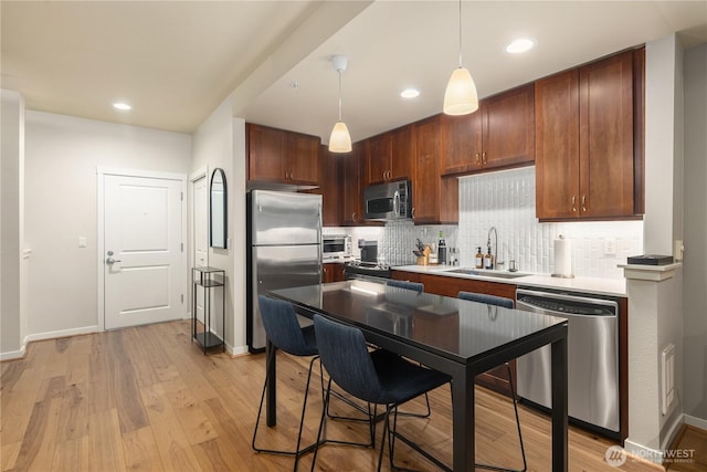 kitchen featuring a sink, stainless steel appliances, hanging light fixtures, and light countertops