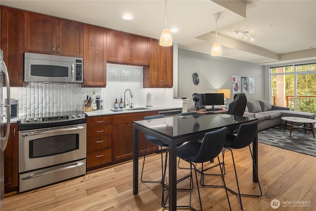 kitchen with light wood-style flooring, a sink, hanging light fixtures, appliances with stainless steel finishes, and light countertops