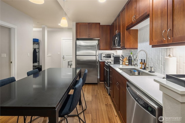 kitchen with stainless steel appliances, light countertops, light wood-style floors, a sink, and a kitchen bar