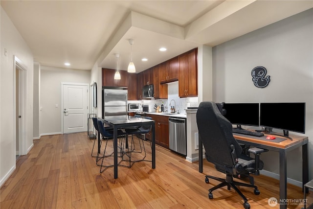 kitchen featuring light wood finished floors, hanging light fixtures, stainless steel appliances, light countertops, and a sink