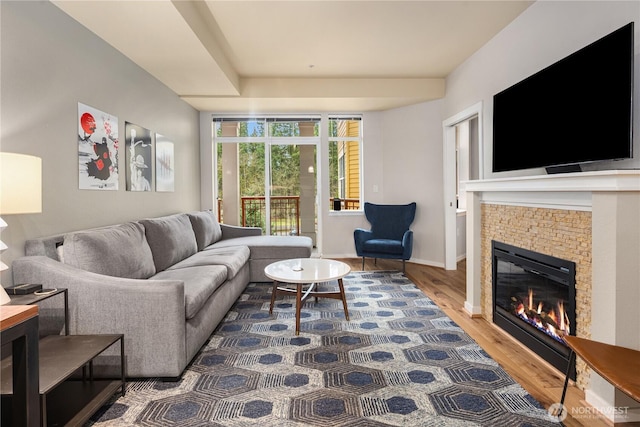 living area featuring a tile fireplace, baseboards, and wood finished floors