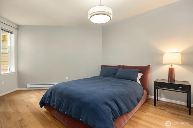 bedroom featuring a baseboard heating unit, baseboards, and light wood finished floors