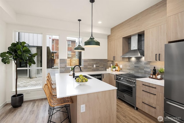 kitchen featuring light brown cabinets, a sink, appliances with stainless steel finishes, wall chimney range hood, and modern cabinets