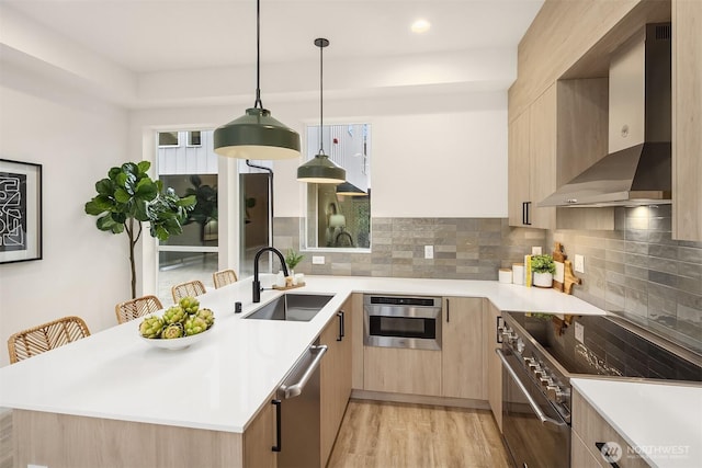 kitchen with wall chimney exhaust hood, light brown cabinets, appliances with stainless steel finishes, and a sink