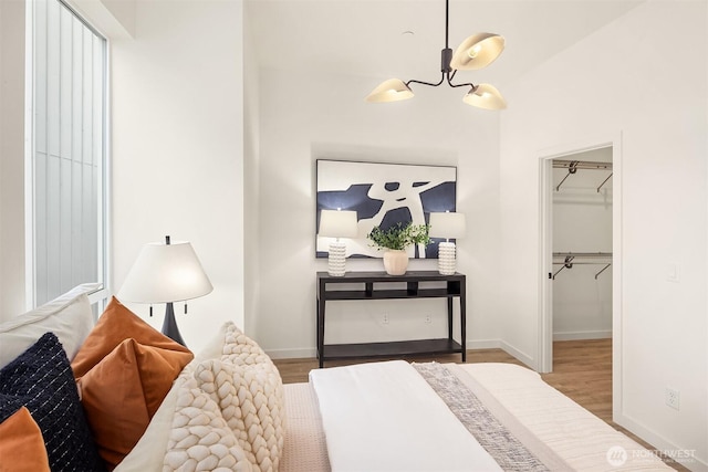 bedroom with a walk in closet, baseboards, wood finished floors, a closet, and a notable chandelier