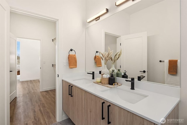 full bath with a sink, baseboards, wood finished floors, and double vanity