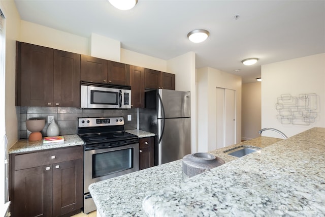 kitchen featuring dark brown cabinetry, backsplash, stainless steel appliances, and a sink