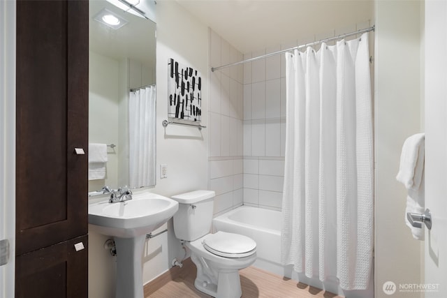 bathroom with wood finished floors, a sink, toilet, and shower / bathtub combination with curtain