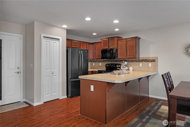 kitchen with a peninsula, a sink, light countertops, backsplash, and black appliances