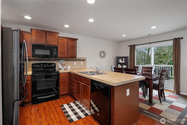 kitchen with a peninsula, dark wood-type flooring, a sink, light countertops, and black appliances