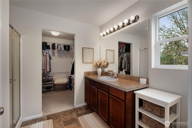 full bathroom featuring a walk in closet, a stall shower, stone finish floor, vanity, and baseboards