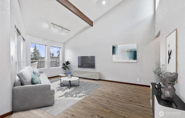 living room featuring hardwood / wood-style floors, track lighting, high vaulted ceiling, and beam ceiling