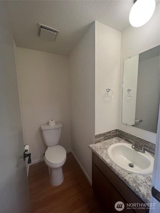 bathroom featuring wood-type flooring, vanity, a textured ceiling, toilet, and decorative backsplash